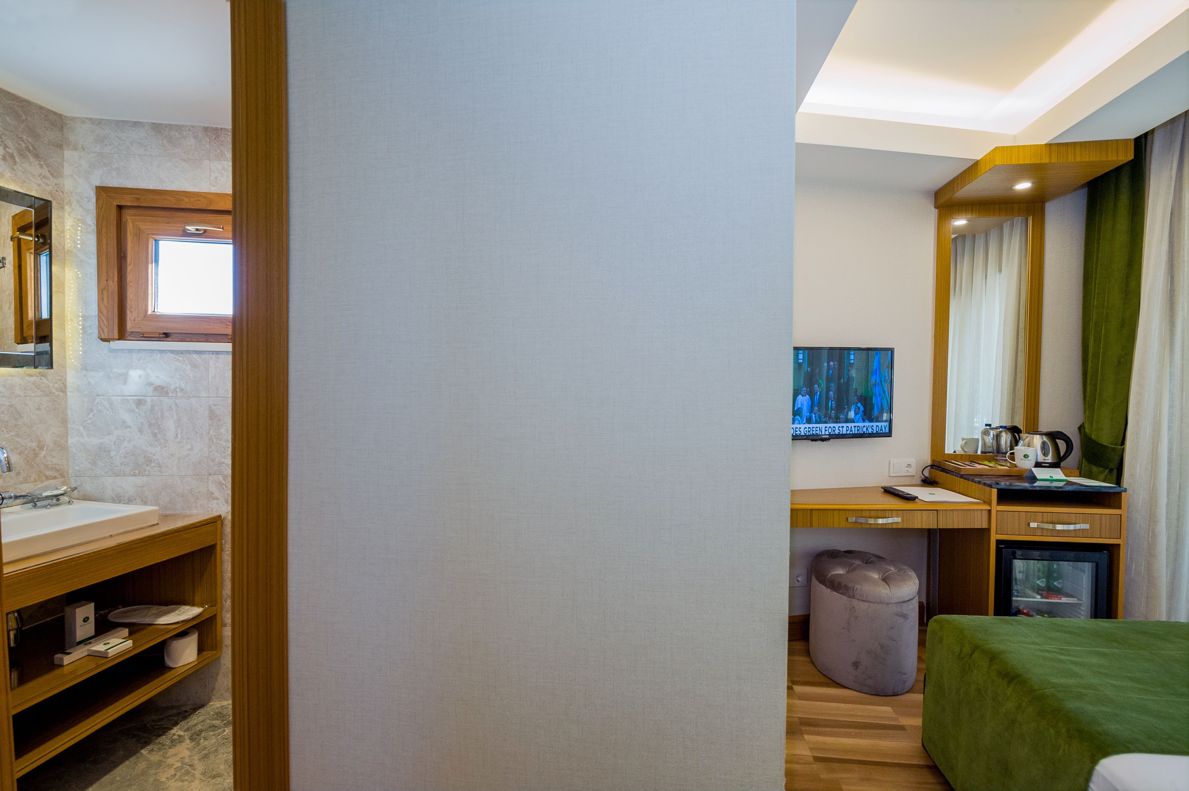 A hotel room with a bathroom, a desk, a bed, and a television.
