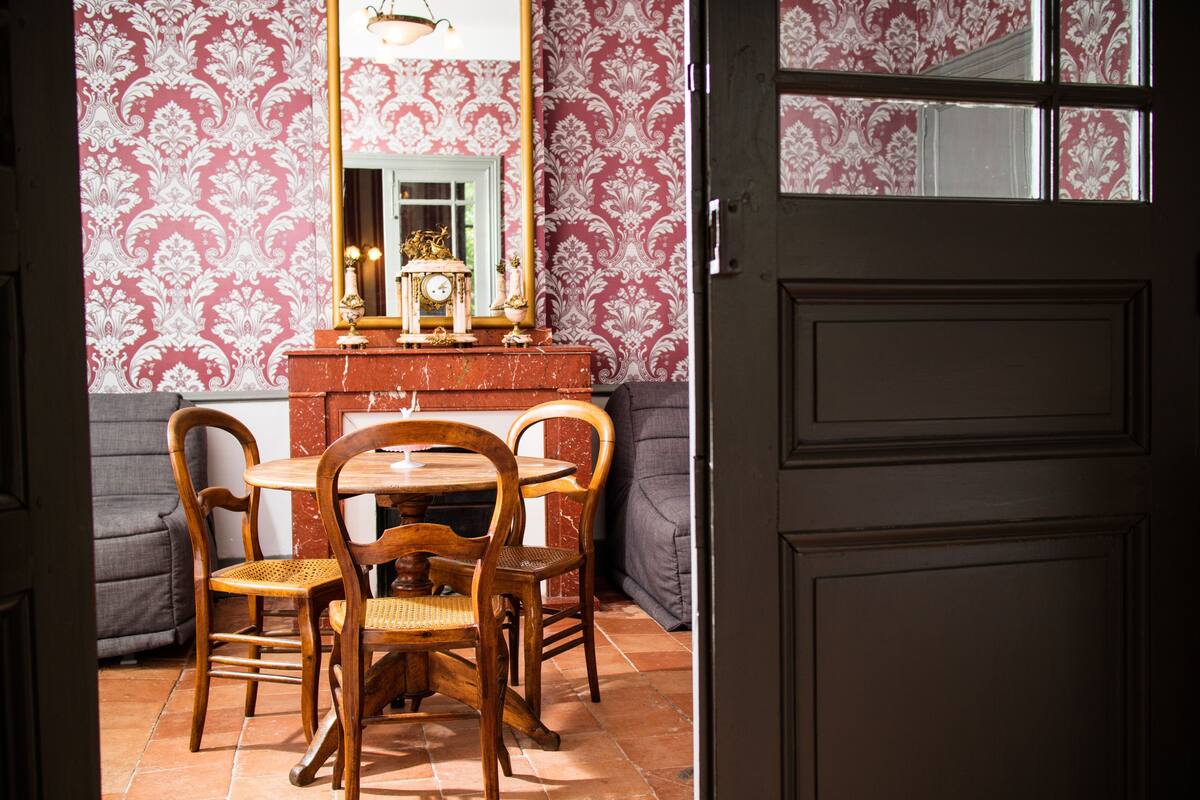 A dining area with a wooden table and chairs, a mirror, and a patterned wallpaper.