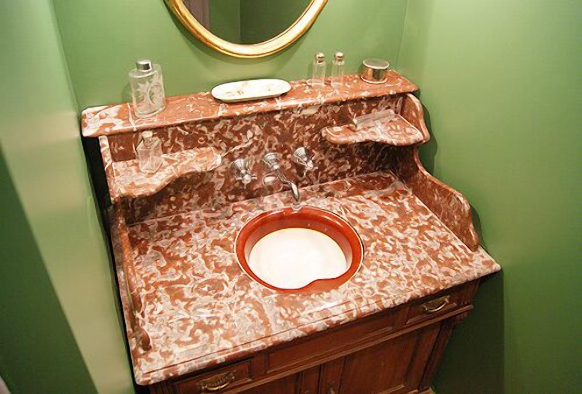 Un baño con lavamanos de mármol, paredes verdes y un espejo con marco dorado.