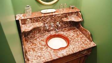 Un baño con lavamanos de mármol, paredes verdes y un espejo con marco dorado.