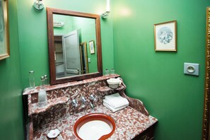 A bathroom with a green wall, a marble sink, a mirror, and a framed picture.