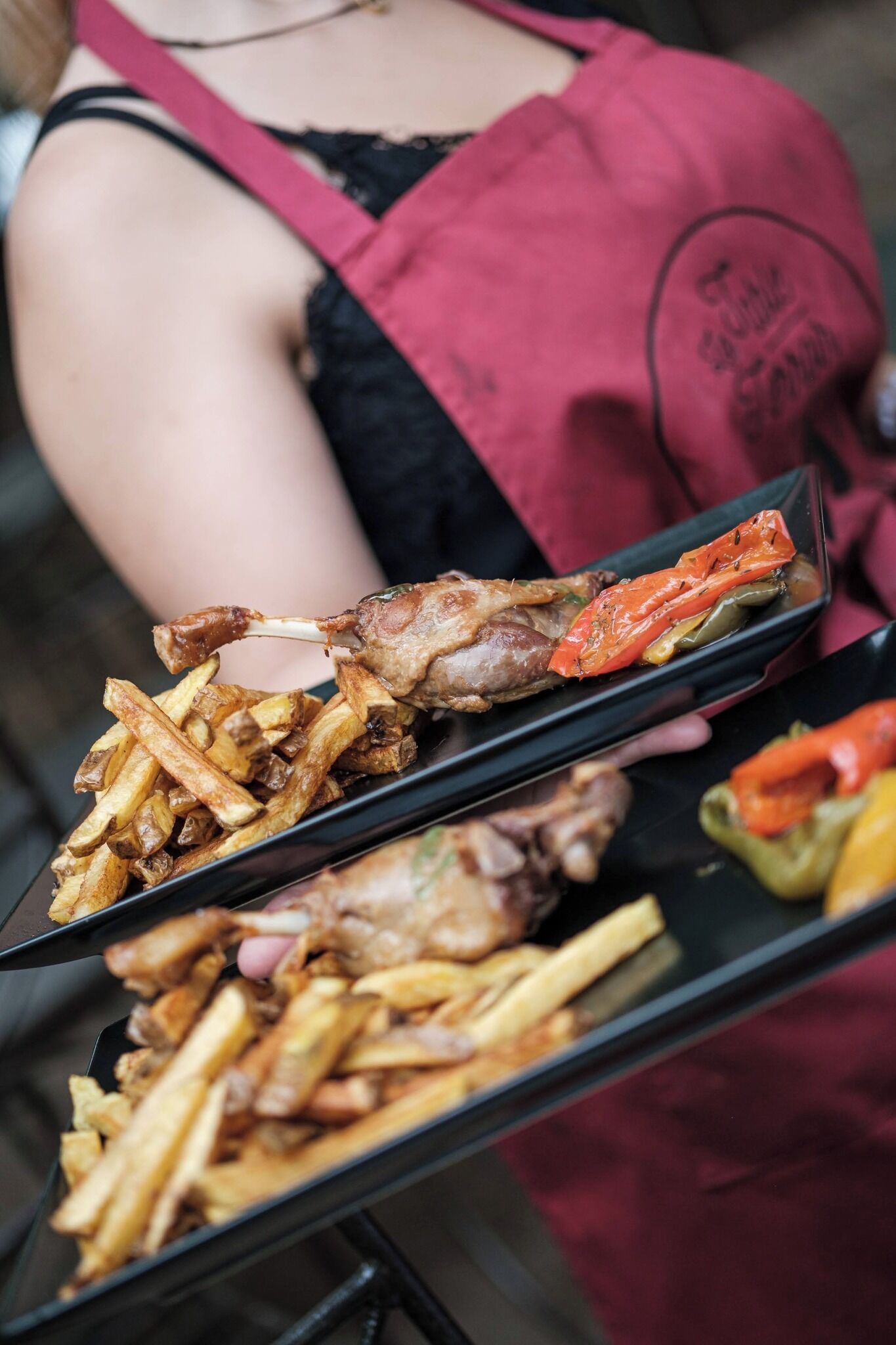 En person holder en bakke med mad, herunder pommes frites og ristede grøntsager.