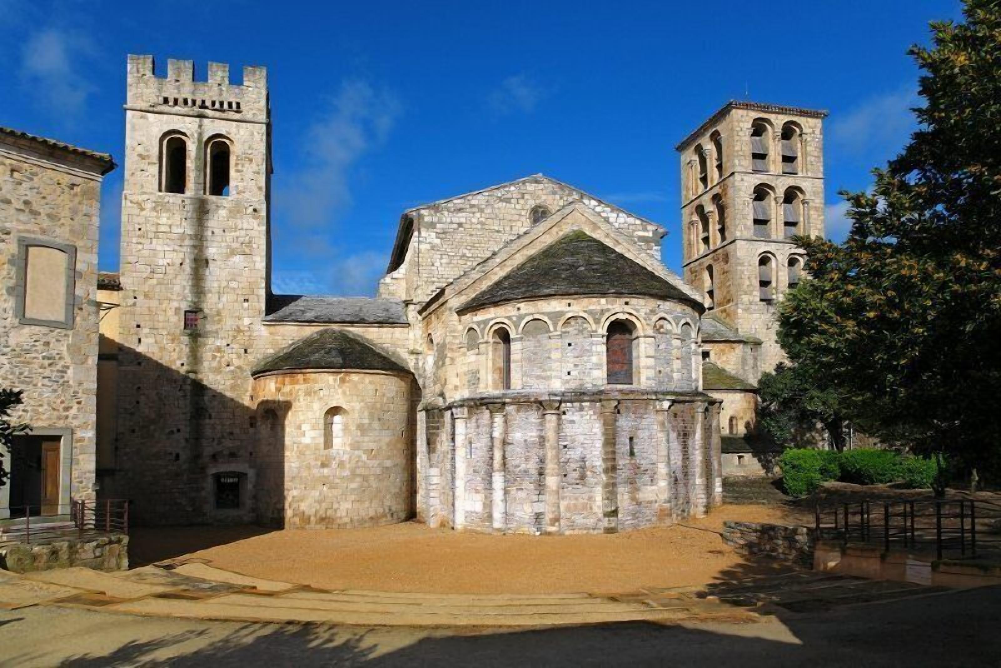 Un edificio histórico de piedra con una torre central, una torre adyacente más pequeña y una estructura circular con ventanas de arco.