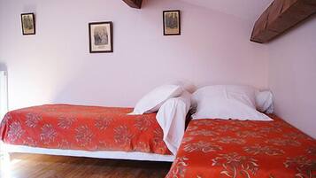 Quarto com duas camas, cada uma com colcha floral vermelha e travesseiros brancos. Há três quadros na parede.