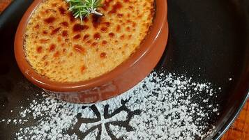 Een schaal crème brûlée op een zwart bord, bestrooid met poedersuiker.