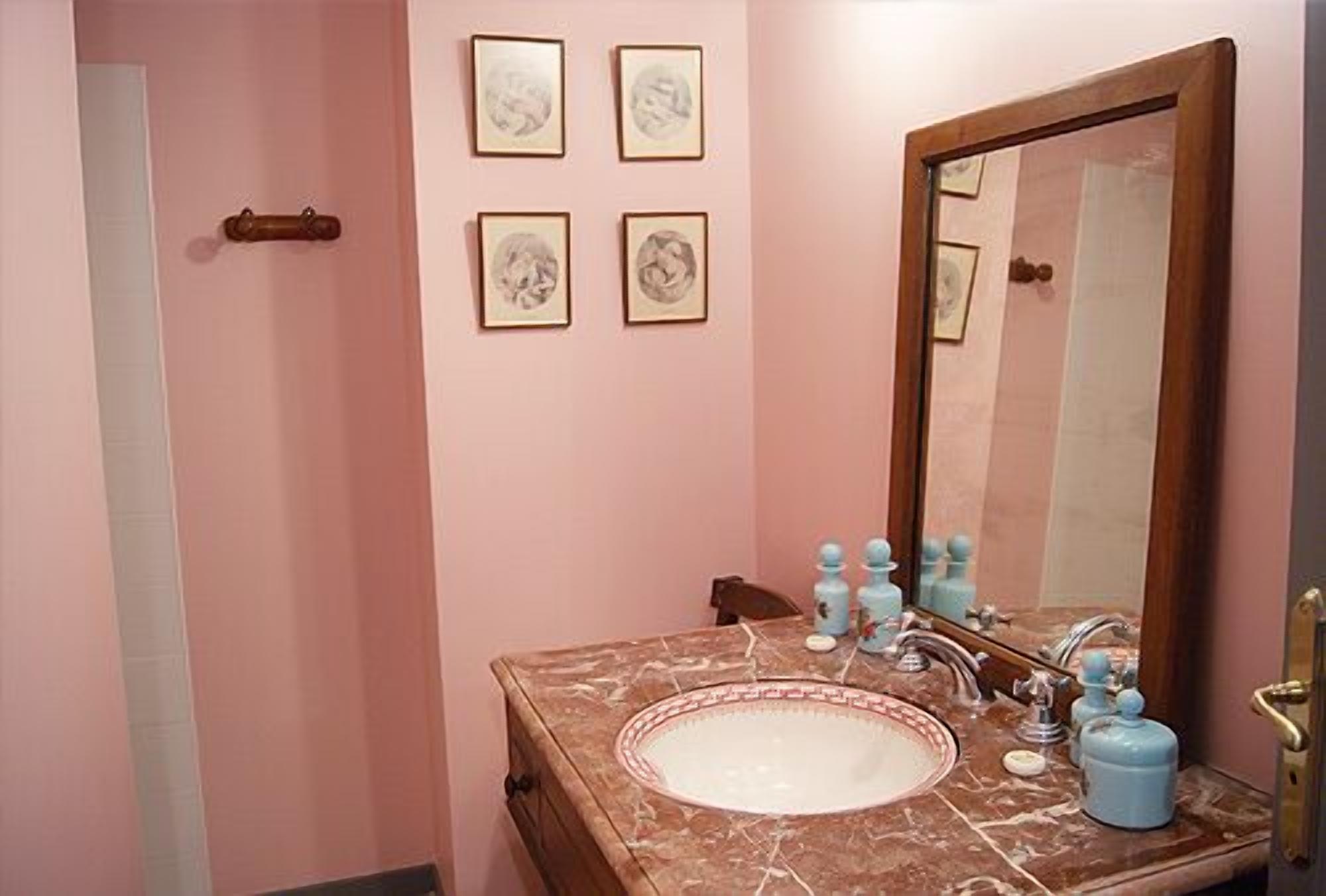 A bathroom with a marble sink, a large mirror, and four framed pictures on the wall.