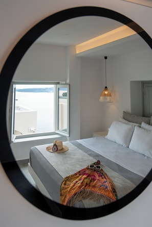 Ein Schlafzimmer mit einem großen Bett, einem Fenster mit Meerblick, einer Hängelampe und einem Spiegel an der Wand.