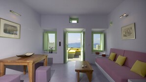 A modern living room with a wooden table, purple ottomans, a pink sofa with yellow cushions, and a view of the sea through a doorway. - Caldera Cliff Illusion Suites (Santorini)