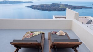 Two wooden lounge chairs with cushions and a hat on one, overlooking a calm sea and distant islands.