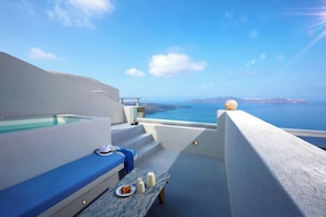 Una terraza con vistas al mar, una mesa con comida y bebidas, y una pared blanca.
