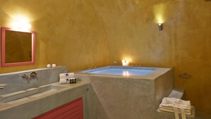 A bathroom with a bathtub, a sink, a mirror, and towels. - Caldera Cliff Illusion Suites (Santorini)