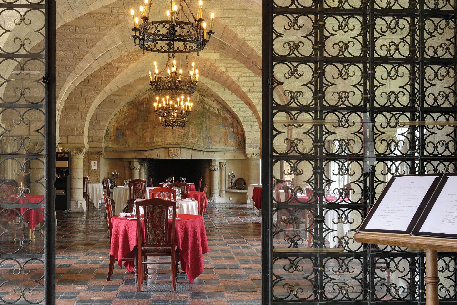 Un comedor interior con mesas dispuestas para el servicio, una araña y un atril para el menú.