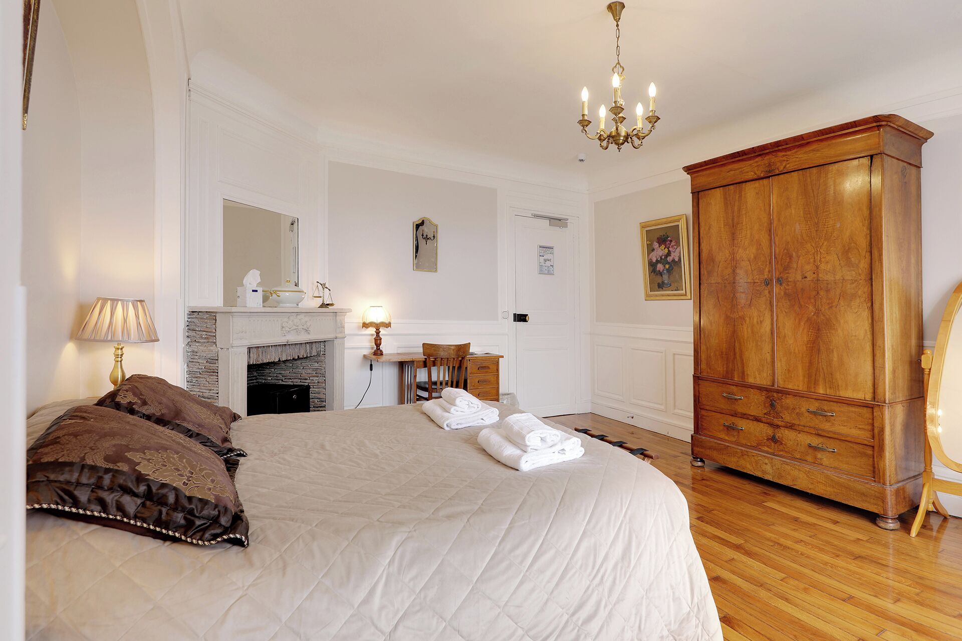 Un dormitorio con una cama grande, un armario de madera, una chimenea y una araña.