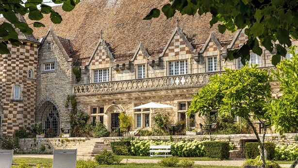 A historic building with a checkered stone facade, a central courtyard with a bench, and a garden with various plants.