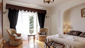 A bedroom with a bed, two armchairs, a small table, and a chandelier.