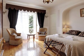A bedroom with a bed, two armchairs, a small table, and a chandelier.
