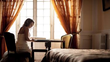 Una stanza con un letto, un tavolo e una sedia. È presente una finestra con tende.