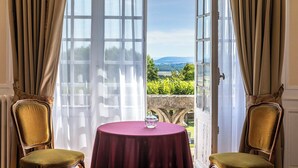 A room with a table and two chairs, a view of a landscape through a large window, and a door with a view of a garden.