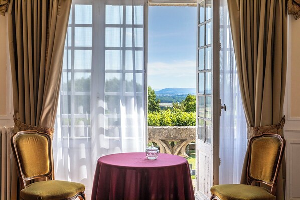 A room with a table and two chairs, a view of a landscape through a large window, and a door with a view of a garden. - Hattonchatel Château & Restaurant La Table du Château (Vigneulles-les-Hattonchatel)