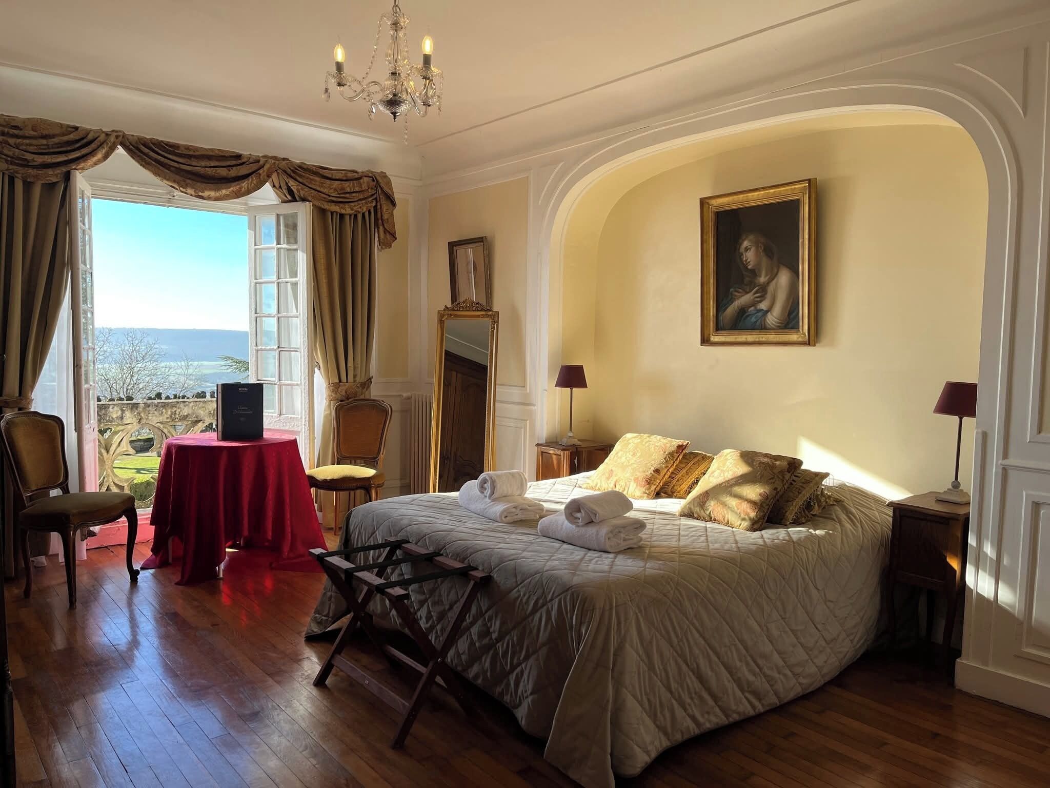 Quarto com uma cama grande, um candelabro, um quadro e vista para o exterior.