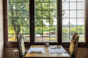 A dining table with two chairs, a window with a grid pattern, and a view of greenery outside.