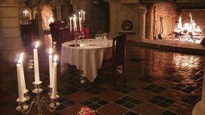 A dimly lit dining area with a stone archway, a fireplace, and a chandelier.