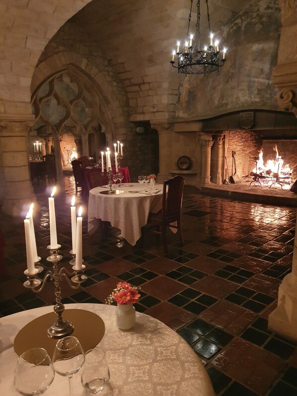 Uma sala de jantar com pouca luz, um arco de pedra, lareira e um candelabro.