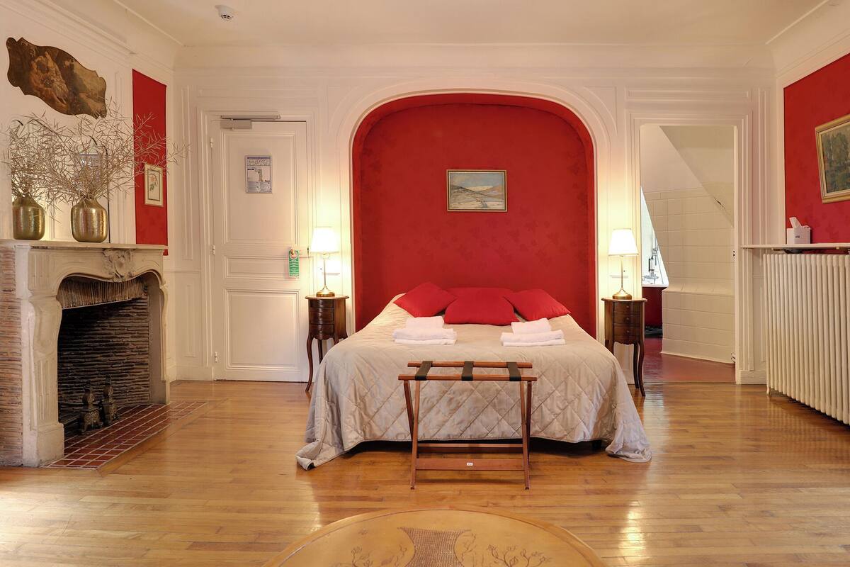 A room with a bed, a fireplace, and a red wall.