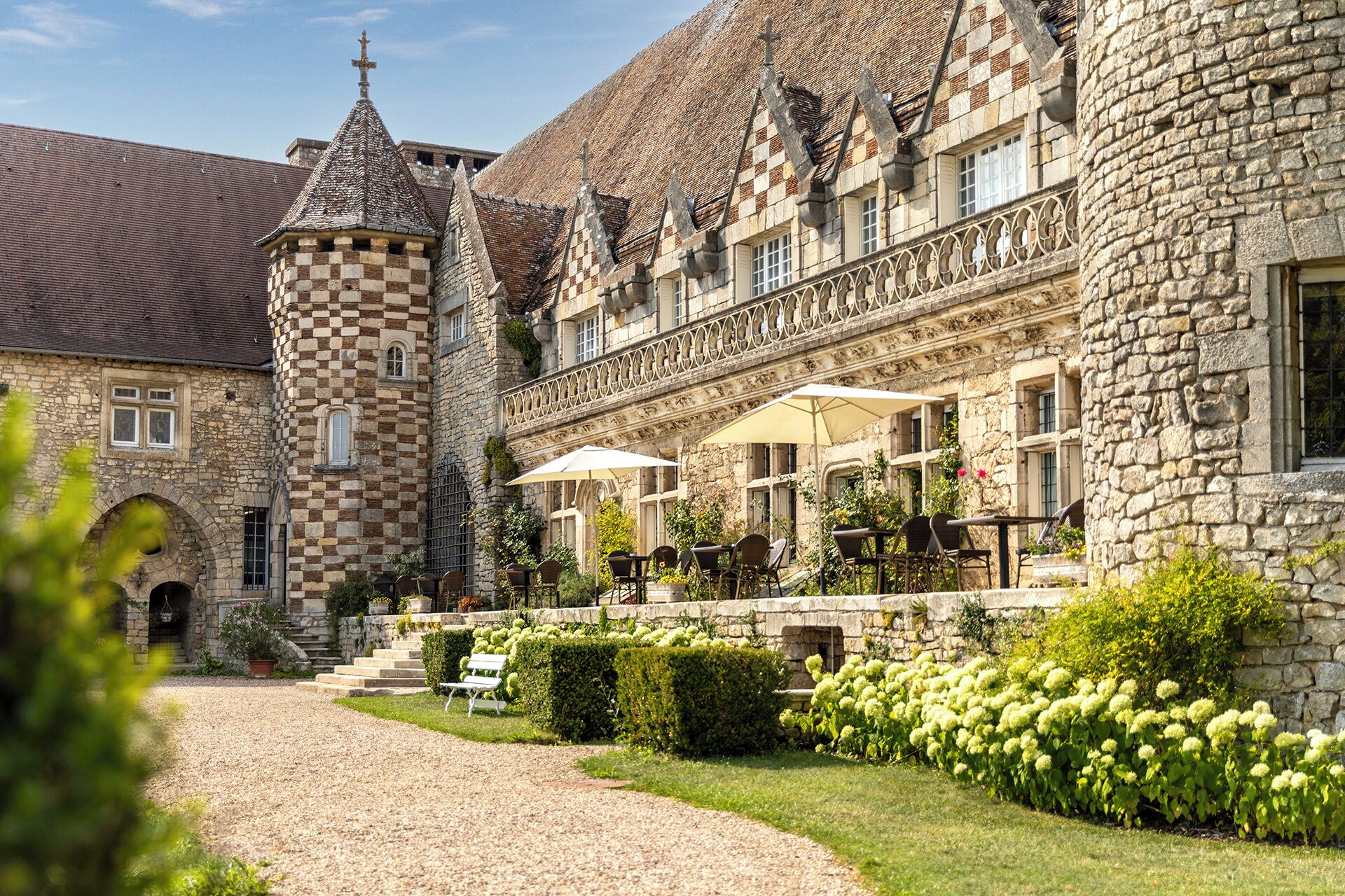 Un edificio histórico de piedra con un patio, mobiliario exterior y una torre.