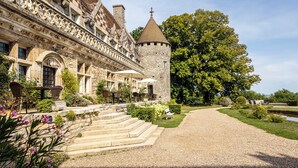 A historic building with a stone tower, a courtyard with outdoor seating, and a large tree.