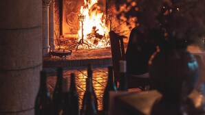 A fireplace with a burning fire, a stone wall, and a chair in front of it.