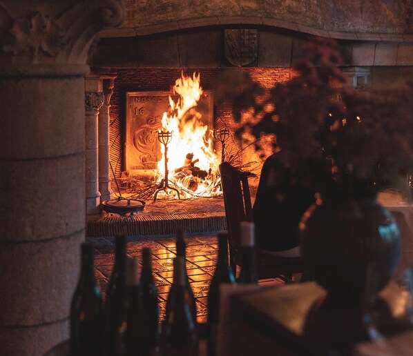 A fireplace with a burning fire, a stone wall, and a chair in front of it. - Hattonchatel Château & Restaurant La Table du Château (Vigneulles-les-Hattonchatel)