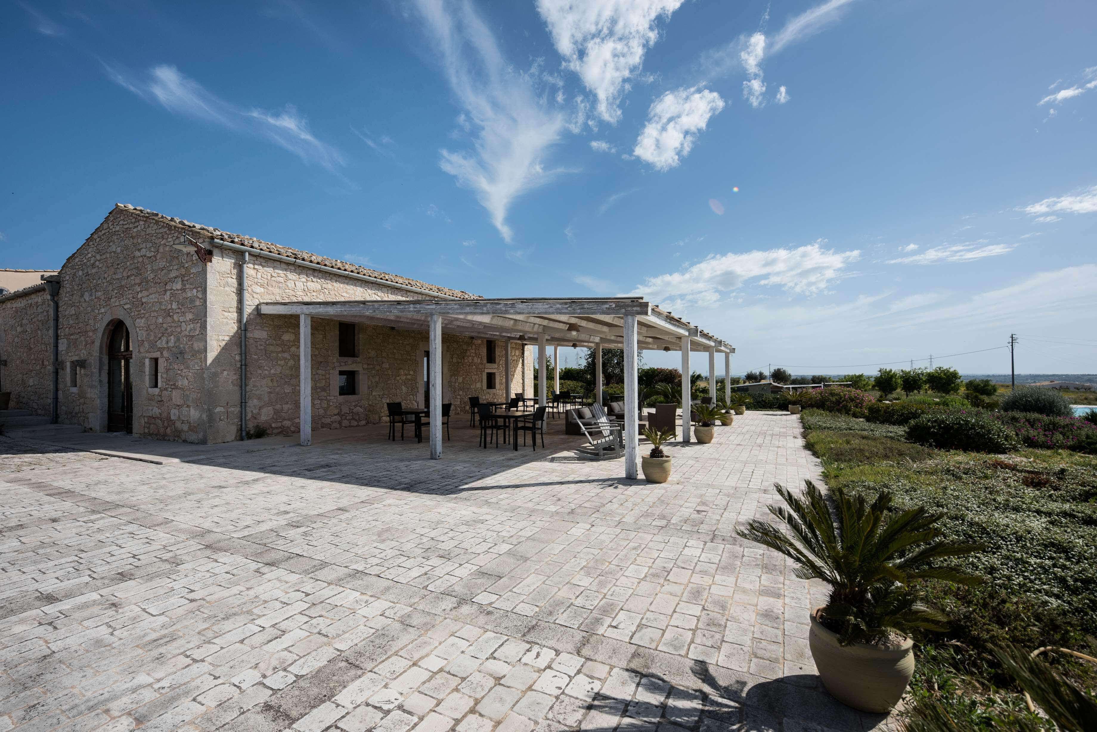 Un edificio de piedra con un patio cubierto, asientos al aire libre y vistas del paisaje.