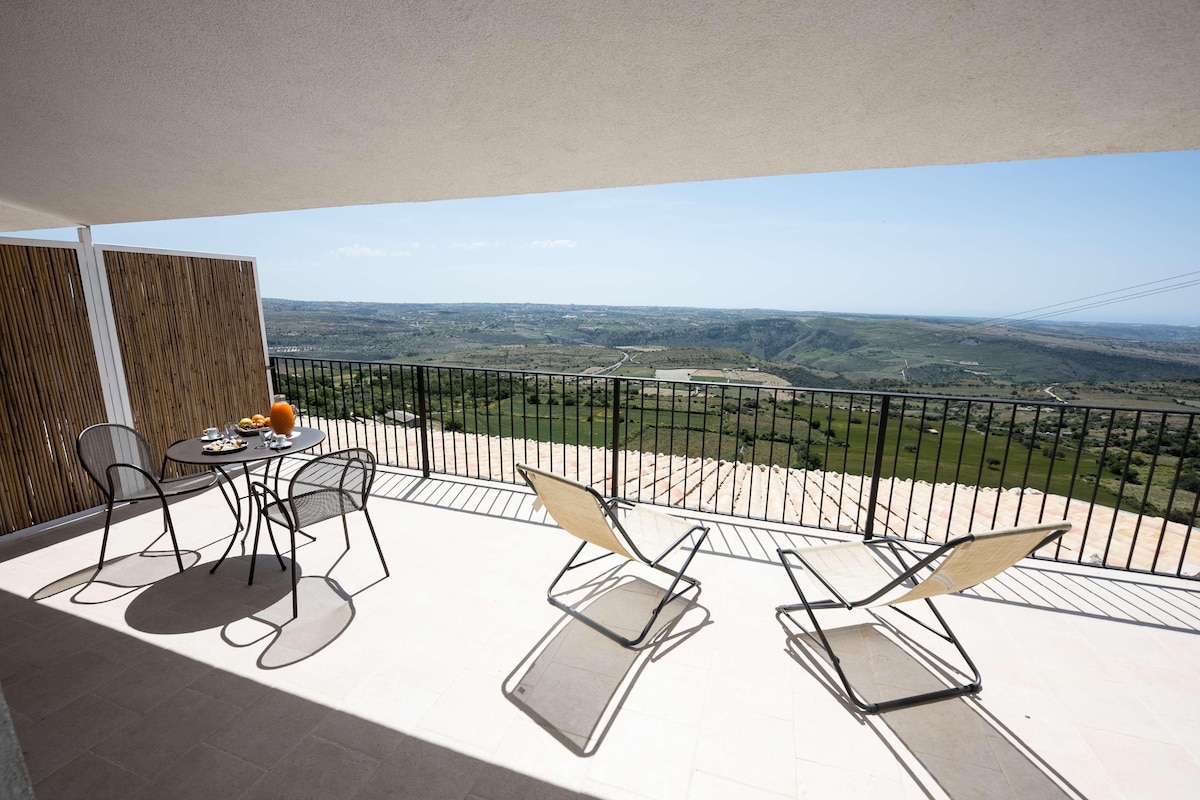 Ein Balkon mit Tisch und Stühlen, Blick auf die Landschaft und eine Holzlattenverkleidung.