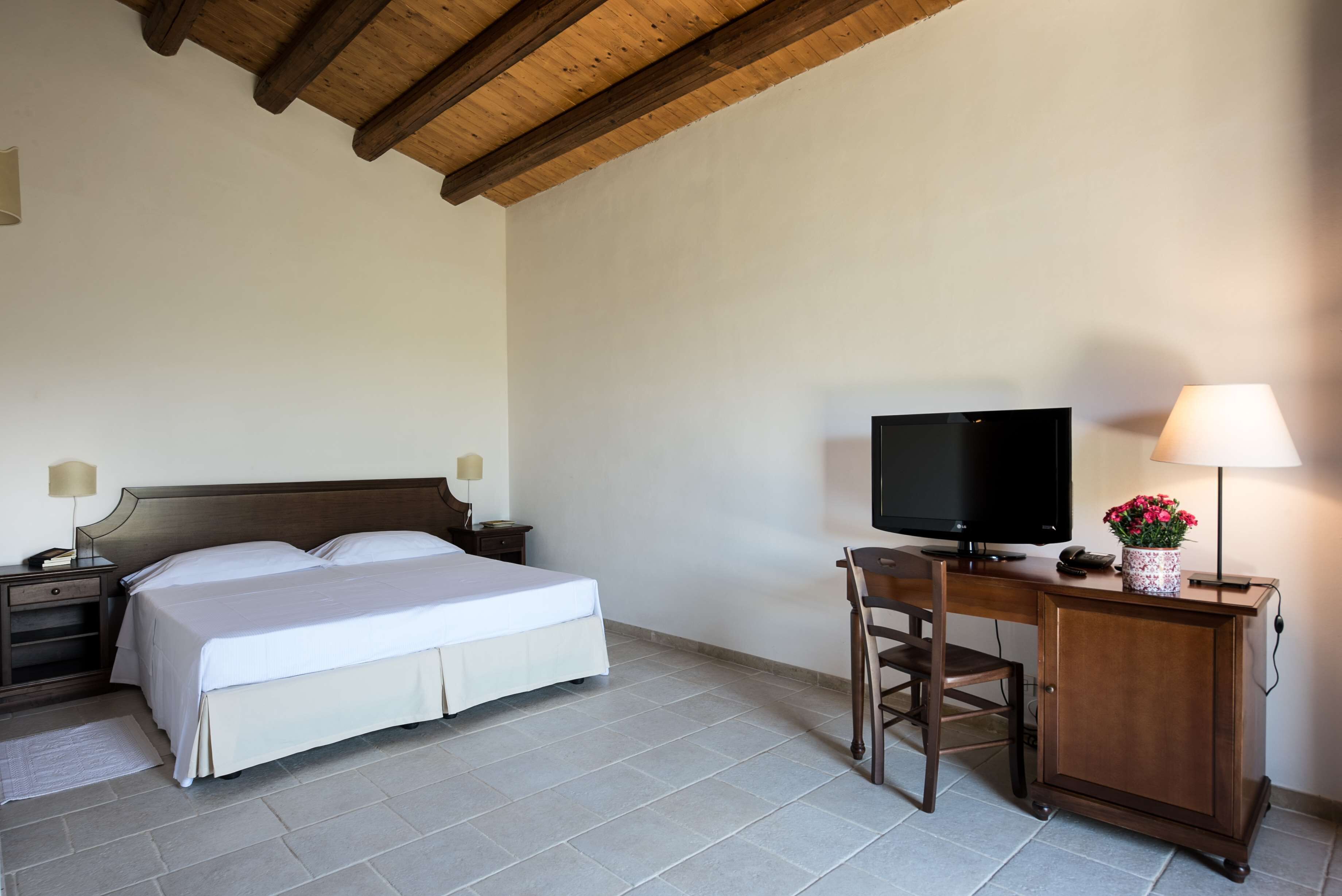 Une chambre à coucher comprenant un lit, un bureau avec une télévision, une chaise et une table de chevet avec une lampe.