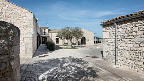 A stone building with a tiled roof, a paved pathway, and a tree in the center. - La Dimora di Spartivento, BW Signature Collection (Ragusa)
