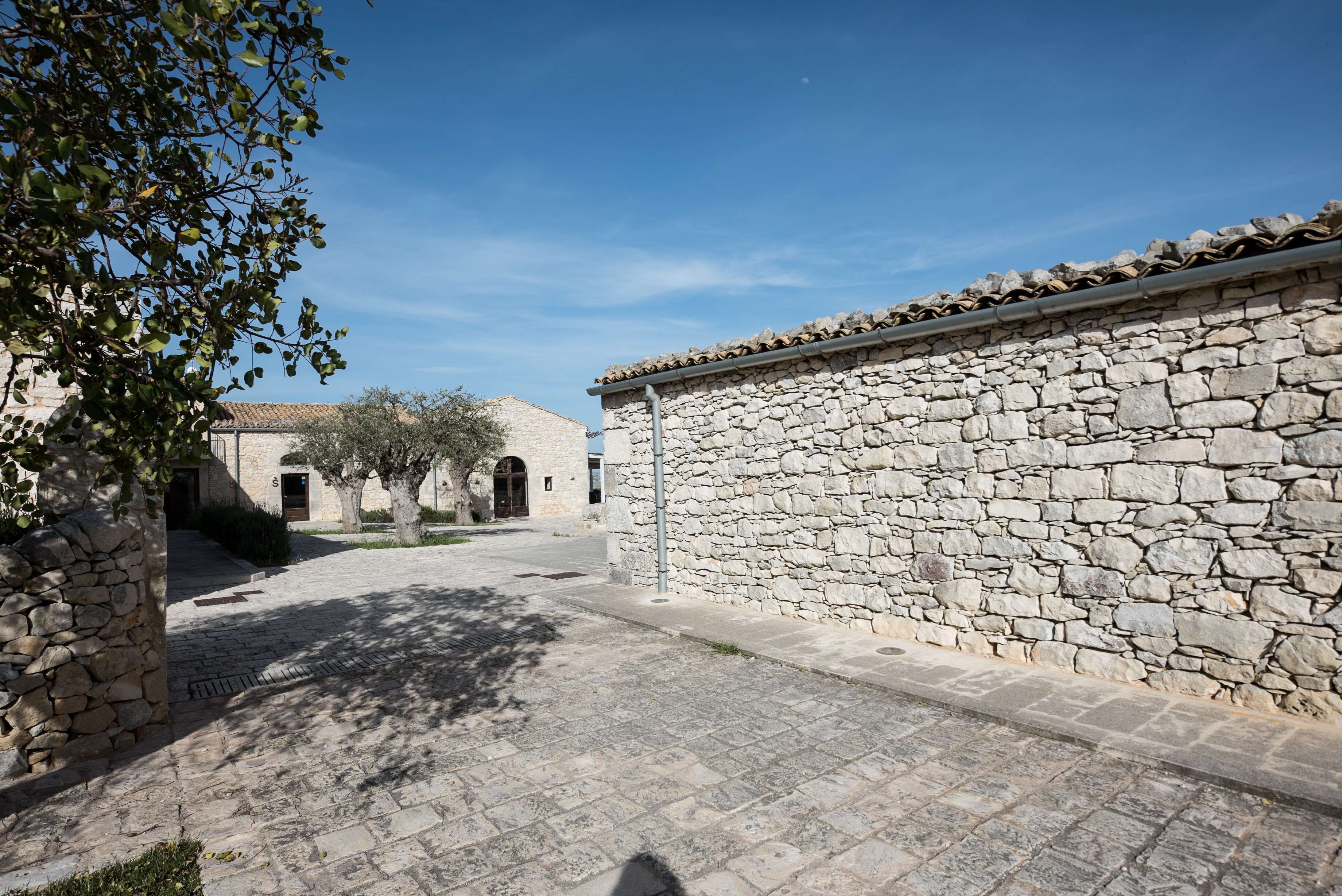 Un patio con paredes de piedra, un sendero pavimentado, un árbol y un edificio con entrada abovedada.
