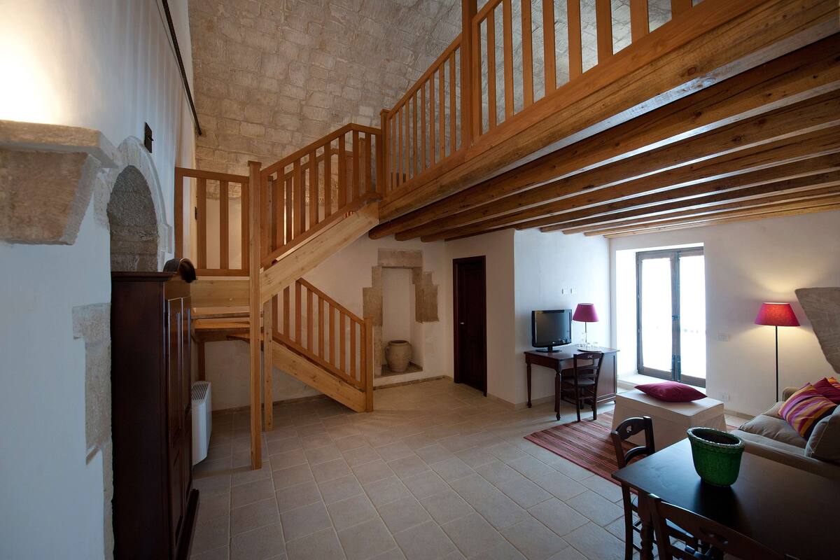 A spacious living area with a wooden staircase, a television, and a cozy seating area with a lamp.