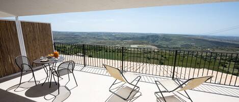 A balcony with a table and chairs, a view of the countryside, and a wooden fence.