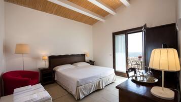 Habitación de hotel con cama, mesitas de noche, una silla roja, un escritorio con lámpara y vistas al exterior.