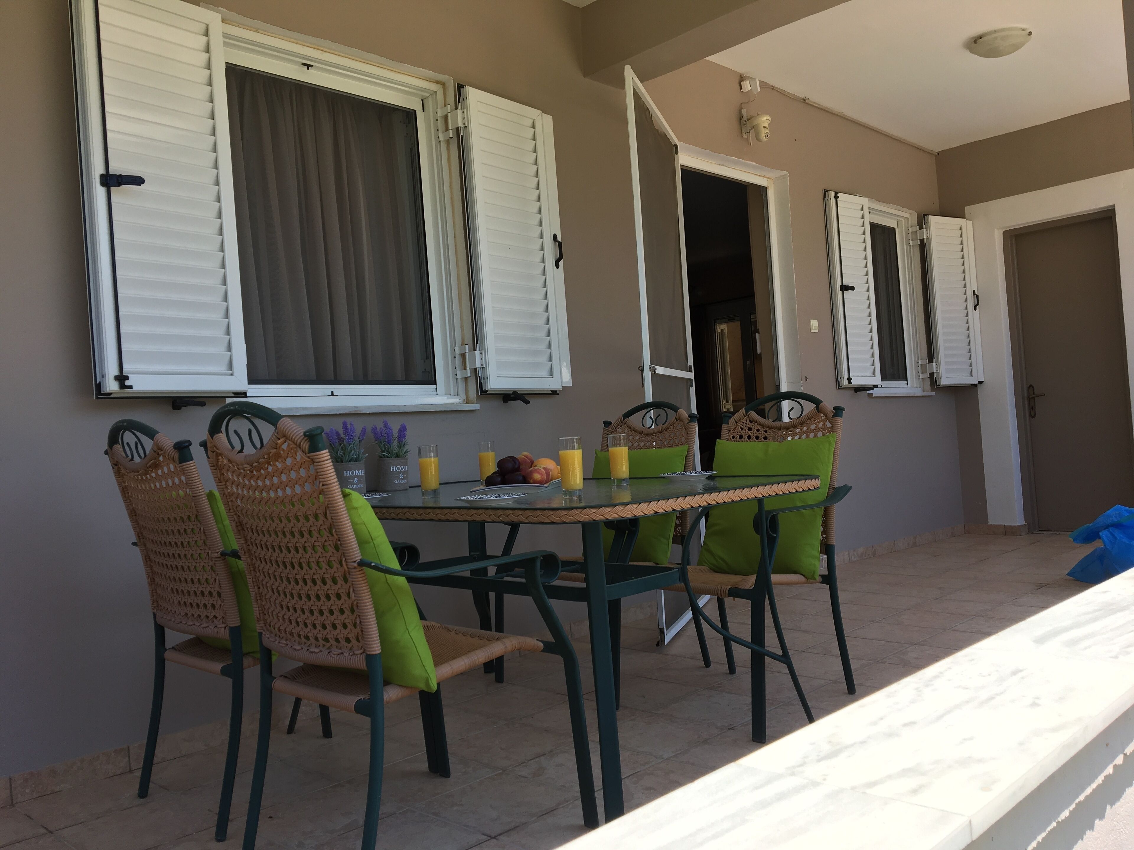 An outdoor dining area with a table and chairs, a window with shutters, and a door.