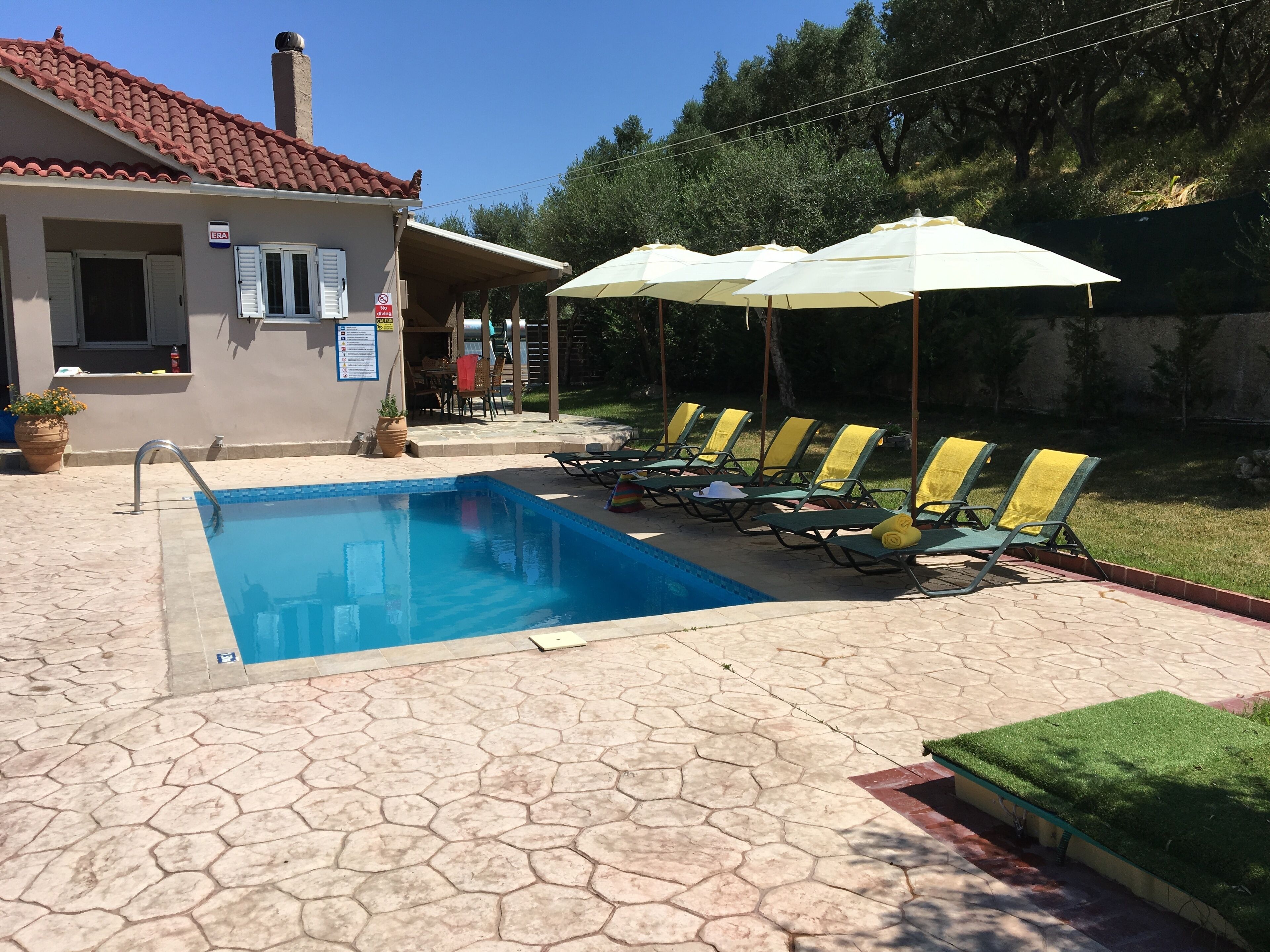 A swimming pool with lounge chairs and umbrellas, a tiled roof, and a small building with a sign.
