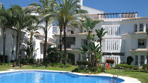 Una piscina rodeada de exuberante vegetación y edificios blancos con balcones.