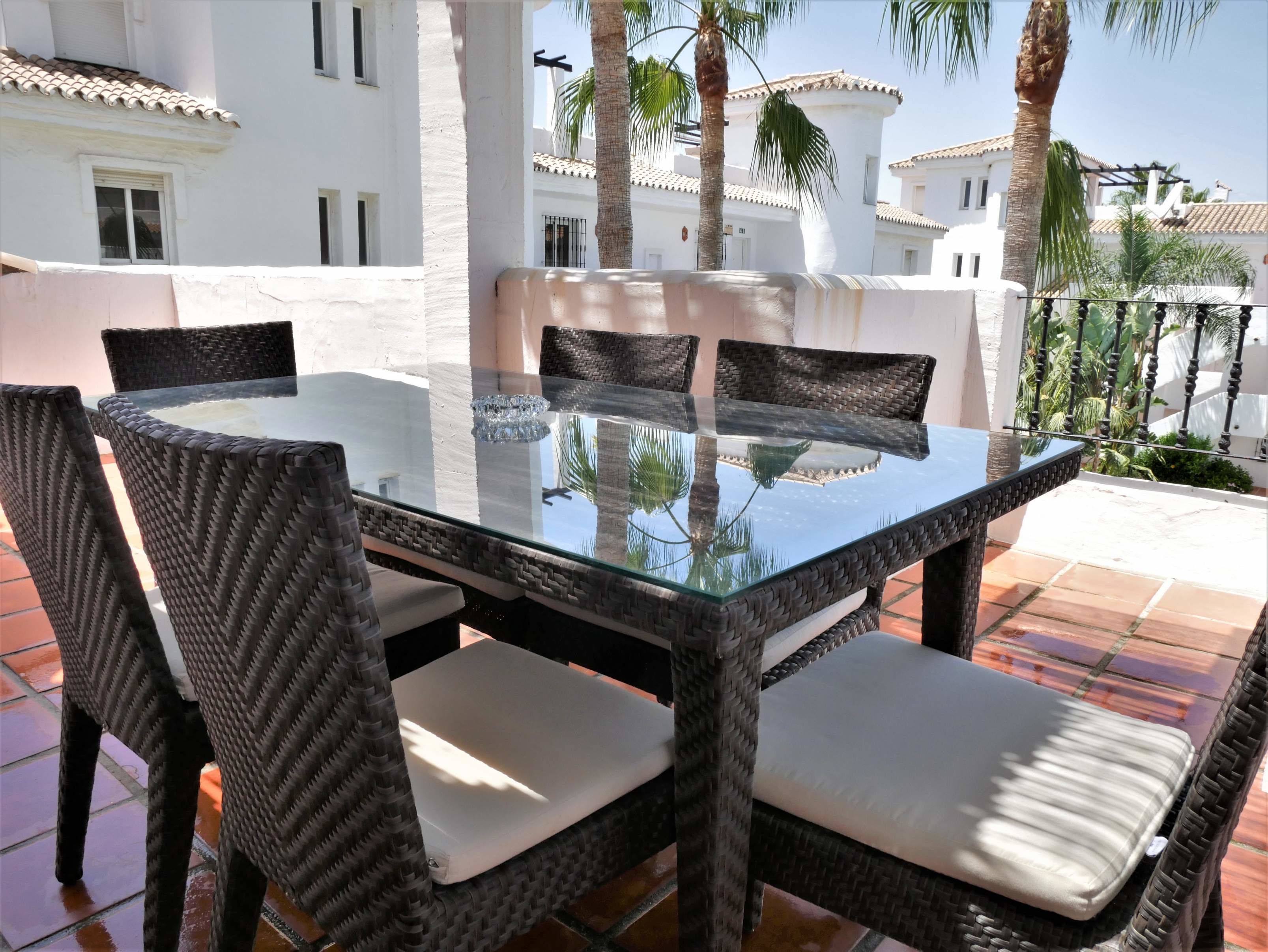 An outdoor dining area with a glass-top table and wicker chairs.