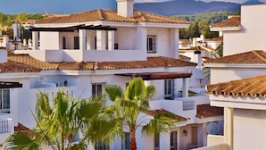 Un edificio blanco con techos de teja terracota, balcones y una palmera en primer plano.