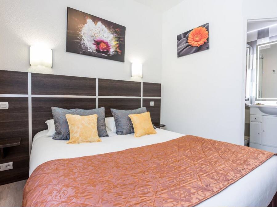 A hotel room with a large bed, a wooden headboard, two wall-mounted lights, and a painting of a flower.