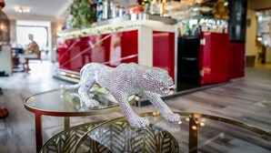 A glass table with a metallic base, a decorative glass sculpture resembling a leopard, and a red and white counter with various items in the background. - Hotel du Centre (Gramat)