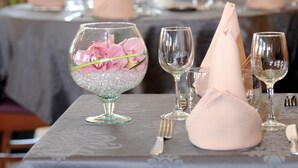A table set for dining with a glass vase containing pink flowers, a folded napkin, and wine glasses. - Hotel du Centre (Gramat)