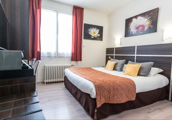 A hotel room with a bed, a TV, a radiator, and a window with curtains.