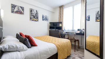 A hotel room with a bed, a desk with a computer, a TV, and artwork on the walls.